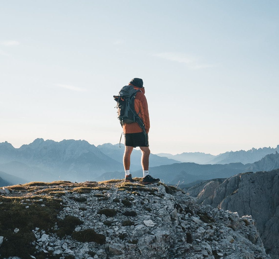 unrecognizable traveler standing on mountain top and admiring landscape