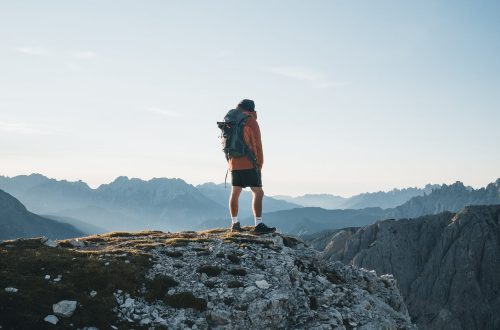 unrecognizable traveler standing on mountain top and admiring landscape